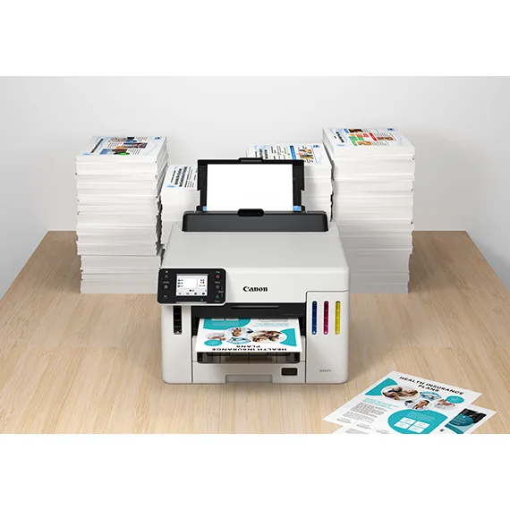 Canon MAXIFY GX5570 on a desk beside stacks of printed paper